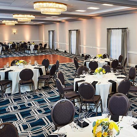 A banquet hall set for a formal event with round tables, yellow floral centerpieces, black chairs, and a patterned carpet.