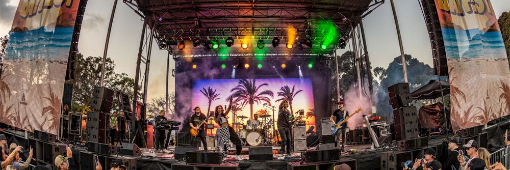 A lively outdoor concert at Mission Bayfest with a big stage, performers, and colorful lights, crowds dancing and enjoying the show.