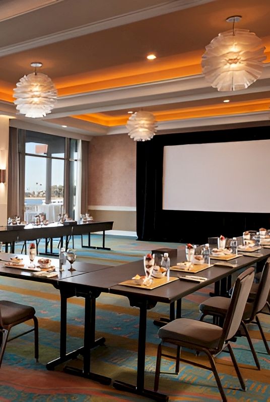 A bright, modern conference room with a U-shaped table setup, large screen, and warm ceiling lighting for meetings or events.