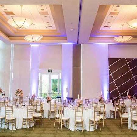 Elegant banquet hall with round tables, white chair covers, soft uplighting, and floral centerpieces for a classy event, ready for guests.