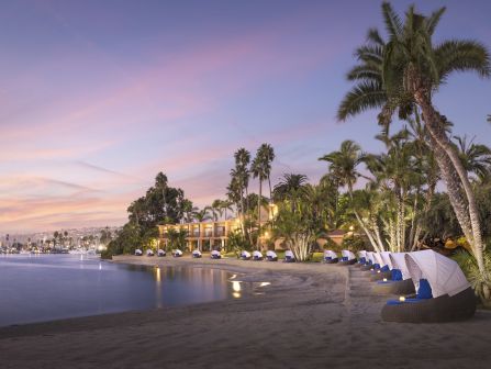 A tranquil beach at sunset with palm trees, lounge chairs, and boats along the shore.