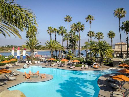 A sunny resort pool scene with palm trees, lounge chairs, umbrellas, and a bright blue pool by the ocean, perfect for a tropical getaway.