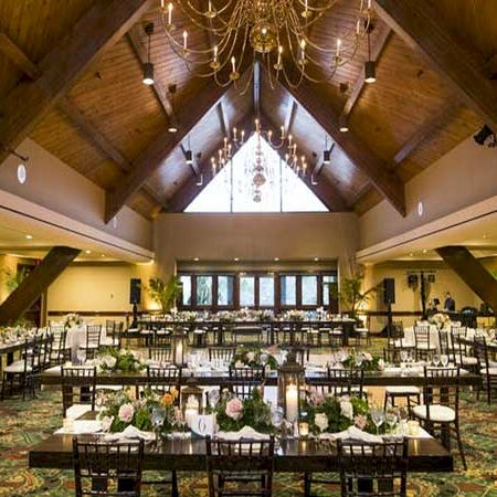 A spacious banquet hall with wooden beams, chandeliers, and long set tables ready for a formal event or wedding reception.