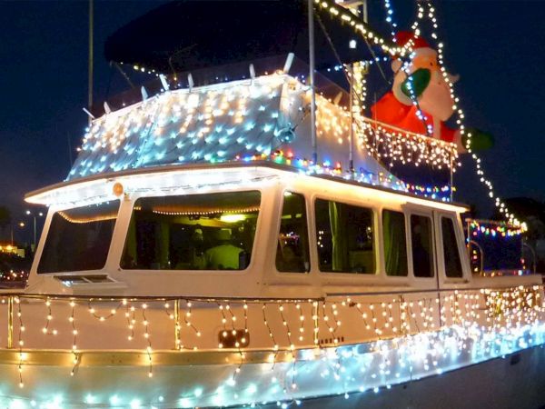 A boat decked out in bright holiday lights, sparkling fairy lights all around, festive decorations on top, against a dark evening sky.