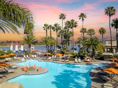 A sunny resort pool scene with palm trees, lounge chairs, and a colorful sunset over the water. (In 140 chars, ends with a period.)