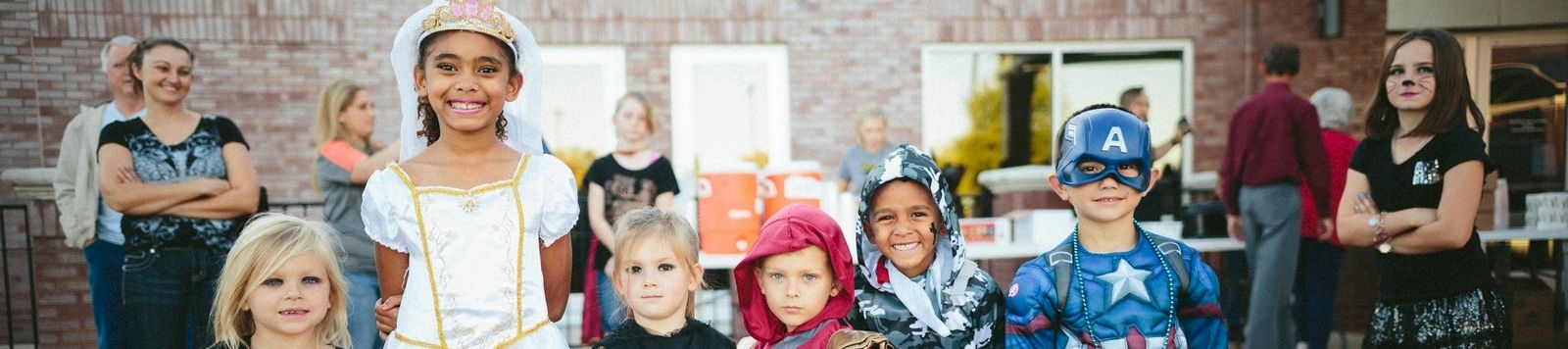 A group of children in Halloween costumes pose together with colorful buckets and jack-o’-lantern buckets, smiling outside.
