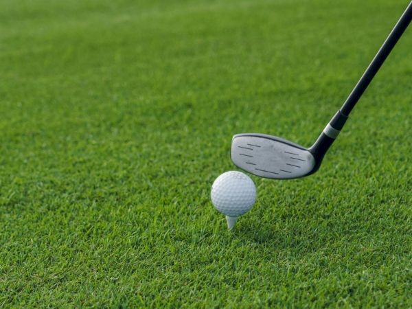A golf ball sits on the green beside a metal club head, ready for the next swing.