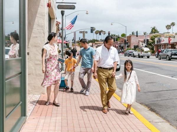 A family strolls down a sunny street in San Francisco Gardens with an American flag overhead.