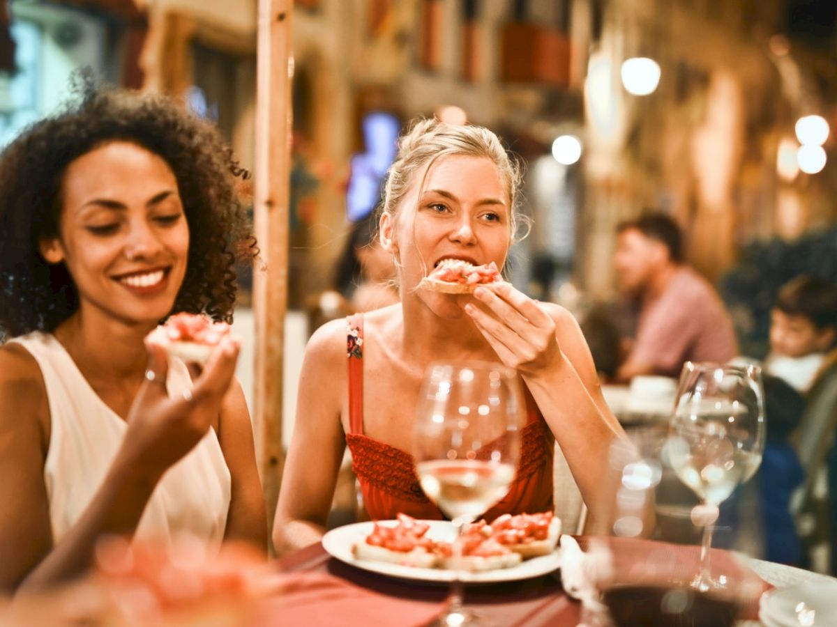 Two women dining at a cozy street cafe, sharing pizza and drinks, smiling as they enjoy a lively evening.