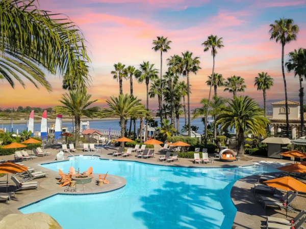 A resort-style pool area with palm trees, lounge chairs, and sunset sky by the sea, perfect for a tropical getaway.