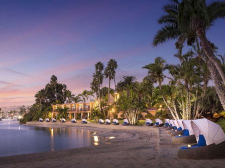 A tropical beach at dusk with calm water, palm trees, and sunshades along the shore, a tranquil resort vibe.
