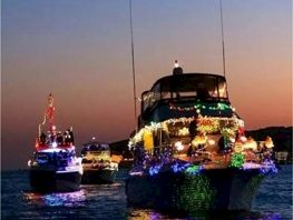 A decorated cruise ship lights up at sunset, with another illuminated boat in a line on the water.