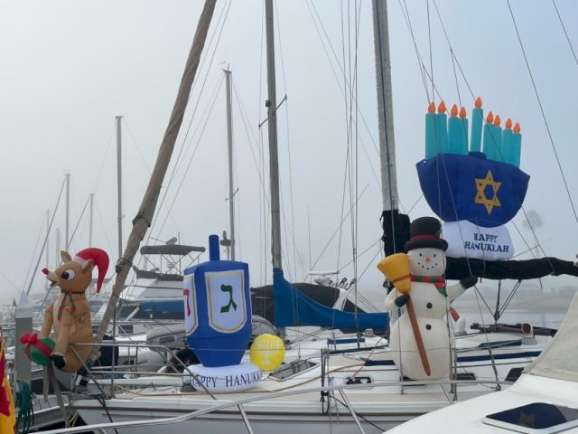 A sailboat deck covered in colorful Hanukkah inflatables&mdash;menorah and snowman&mdash;decorated among the rigging and sails.